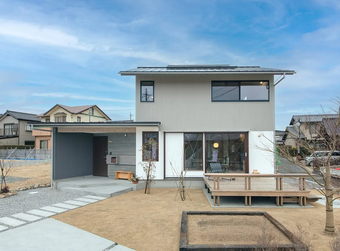 ウッドデッキ付きの庭と大きな窓が特徴のモダンな二階建て住宅